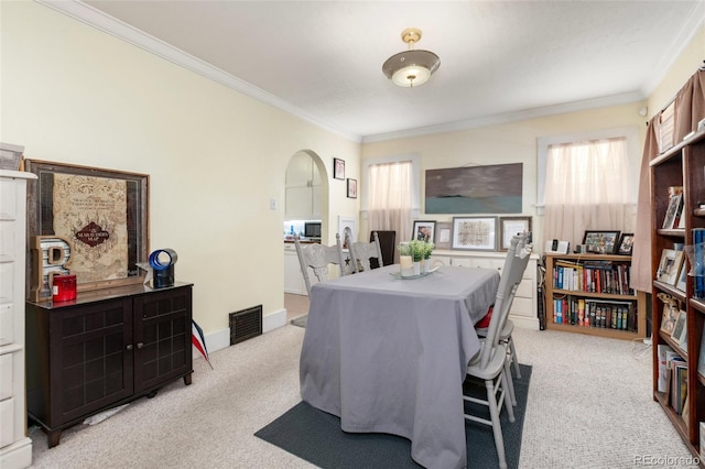dining room featuring light carpet, ornamental molding, and arched walkways