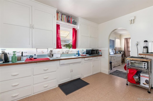 kitchen featuring stainless steel microwave, white cabinets, light floors, and arched walkways