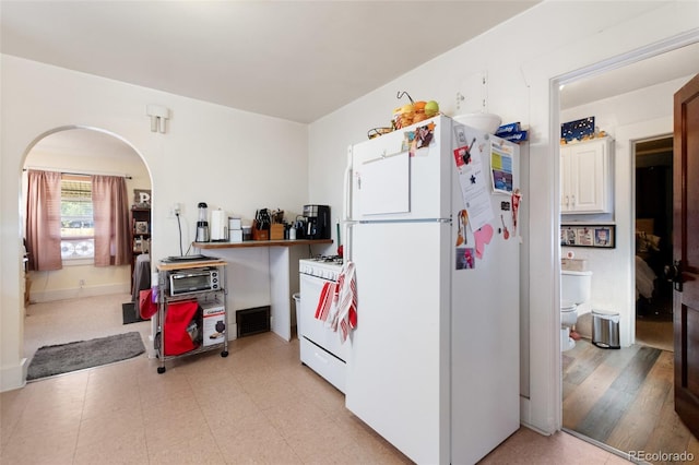 kitchen with white appliances, light flooring, and arched walkways