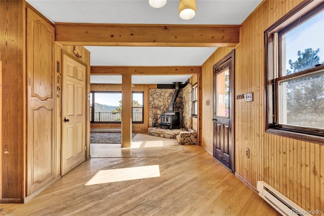 entryway featuring a baseboard radiator, light wood-type flooring, a wood stove, and a healthy amount of sunlight