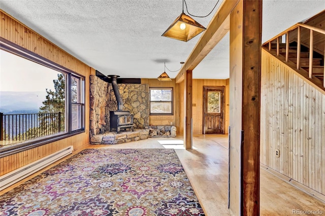 unfurnished living room featuring a textured ceiling, a wood stove, and a baseboard radiator