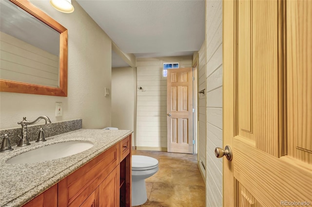 bathroom featuring vanity, wood walls, toilet, and a textured ceiling