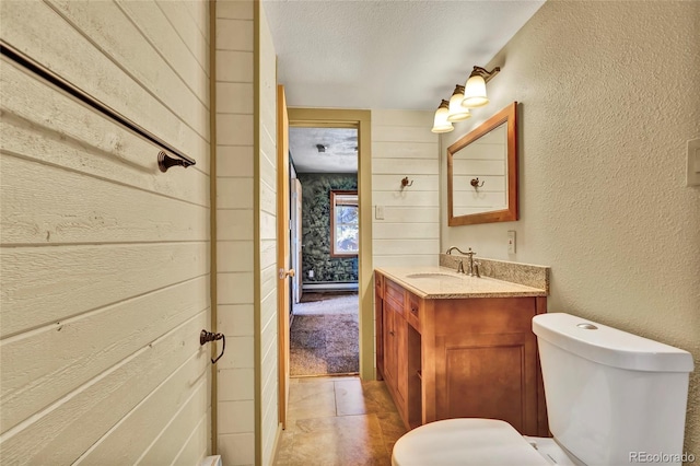 bathroom with vanity, wooden walls, toilet, and a textured ceiling