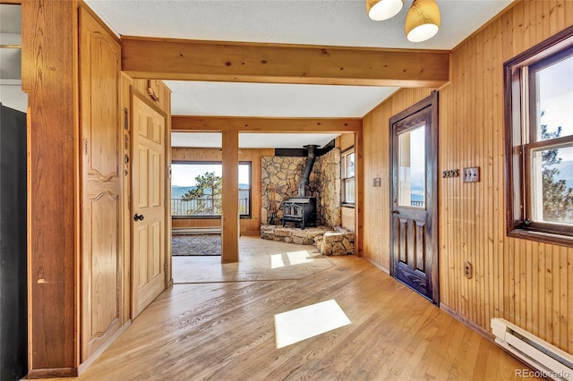 foyer entrance featuring a baseboard radiator, a wood stove, a wealth of natural light, and light wood-type flooring