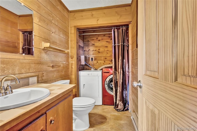 bathroom with washing machine and dryer, wood walls, vanity, a textured ceiling, and toilet