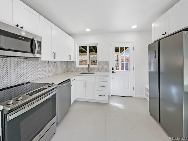 kitchen featuring appliances with stainless steel finishes, backsplash, light tile floors, sink, and white cabinets