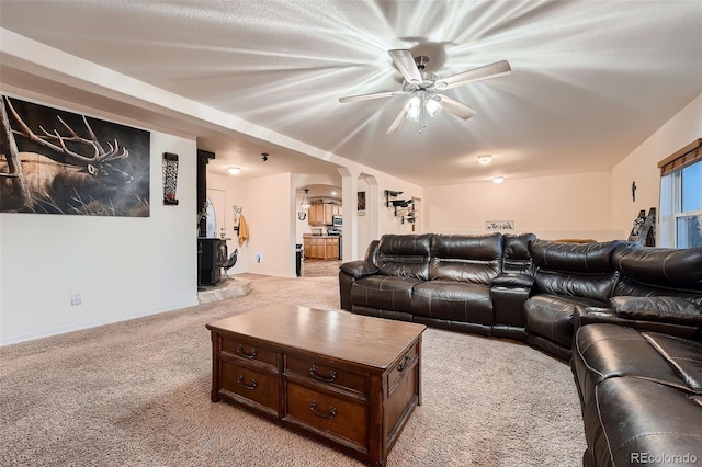 living room featuring light colored carpet, ceiling fan, and a wood stove