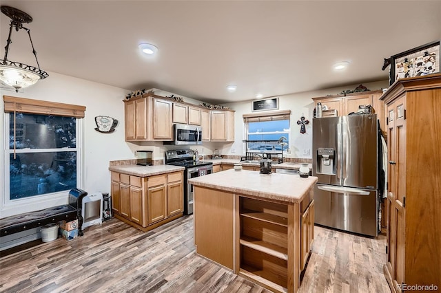 kitchen featuring a kitchen island, decorative light fixtures, stainless steel appliances, light brown cabinets, and light wood-type flooring