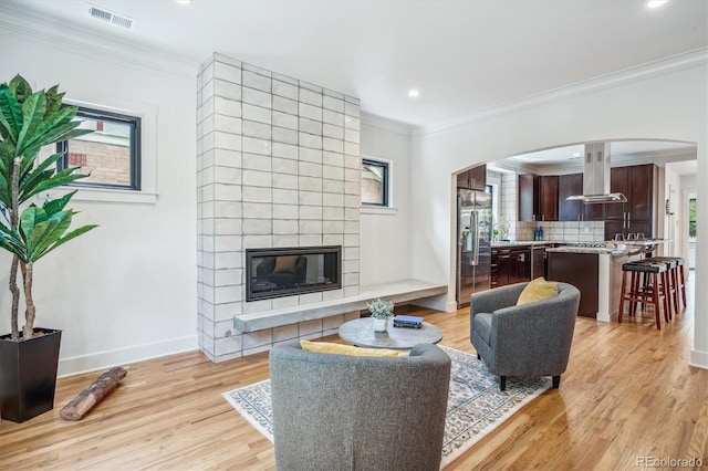 living room with plenty of natural light, a tile fireplace, light hardwood / wood-style flooring, and crown molding