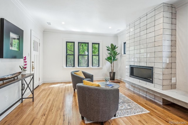 living room with light wood-type flooring, a tiled fireplace, and crown molding