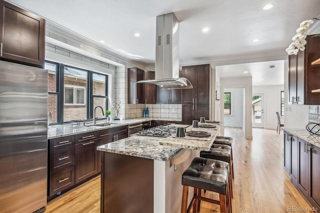 kitchen with island exhaust hood, crown molding, stainless steel appliances, light hardwood / wood-style floors, and a center island