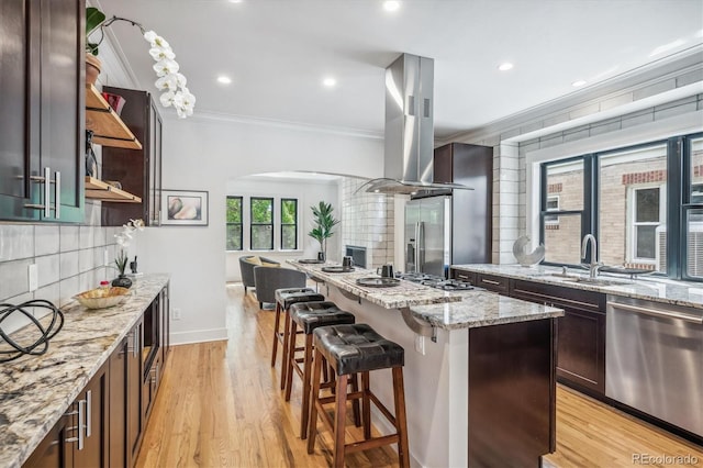 kitchen with sink, island exhaust hood, a kitchen island, light wood-type flooring, and appliances with stainless steel finishes