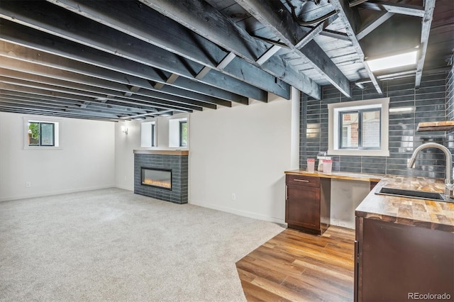 basement with a healthy amount of sunlight, light wood-type flooring, a brick fireplace, and sink