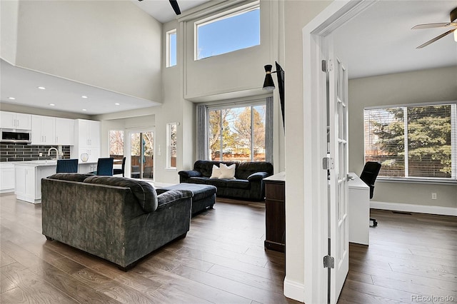 living area with a wealth of natural light, baseboards, dark wood-style flooring, and a ceiling fan