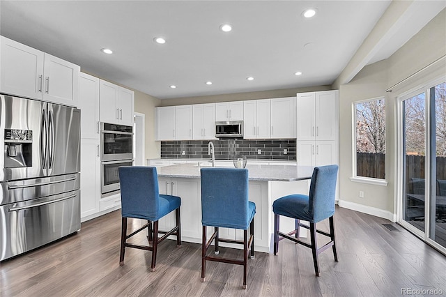 kitchen with an island with sink, dark wood-style floors, appliances with stainless steel finishes, a kitchen breakfast bar, and backsplash