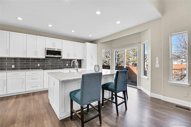 kitchen featuring black stovetop, dark wood finished floors, stainless steel microwave, visible vents, and decorative backsplash