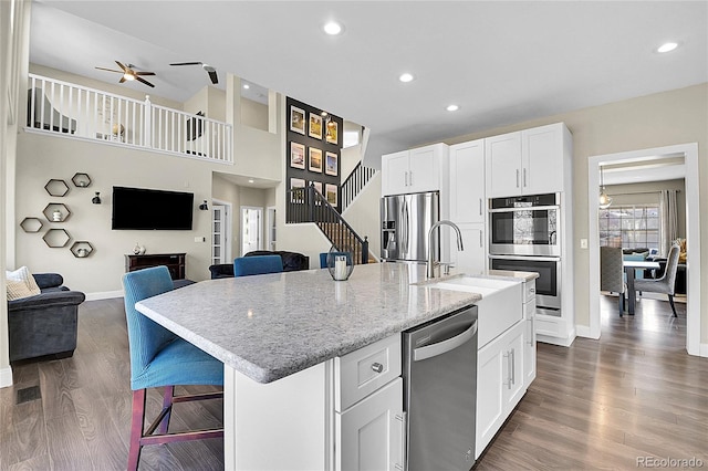 kitchen with dark wood-style flooring, appliances with stainless steel finishes, open floor plan, a kitchen island with sink, and white cabinets