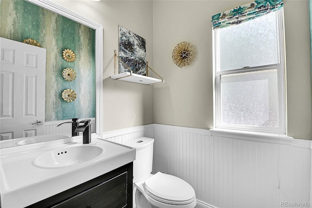 half bathroom with a wainscoted wall, vanity, and toilet