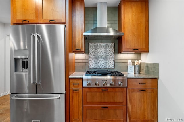 kitchen featuring wall chimney range hood, appliances with stainless steel finishes, tasteful backsplash, and brown cabinets