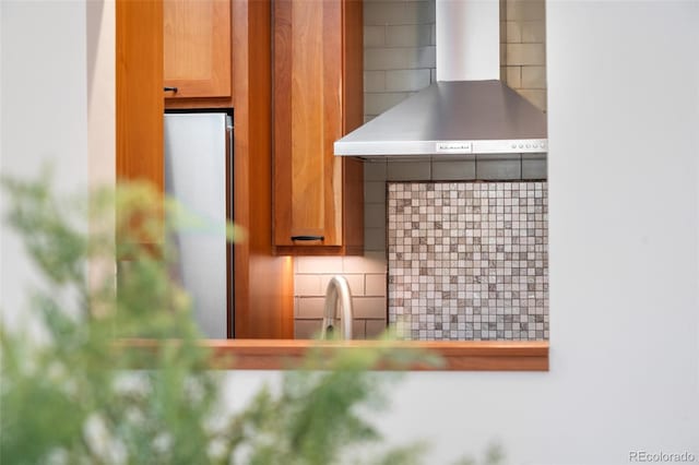 room details with wall chimney range hood, brown cabinetry, decorative backsplash, and a sink