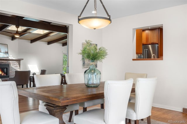 dining room with beamed ceiling, baseboards, wood finished floors, and a fireplace