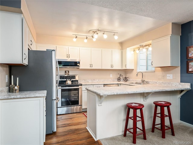 kitchen with a breakfast bar area, a peninsula, a sink, white cabinets, and appliances with stainless steel finishes