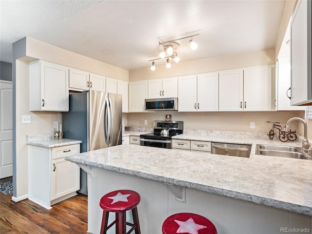 kitchen with a breakfast bar, sink, white cabinets, kitchen peninsula, and appliances with stainless steel finishes