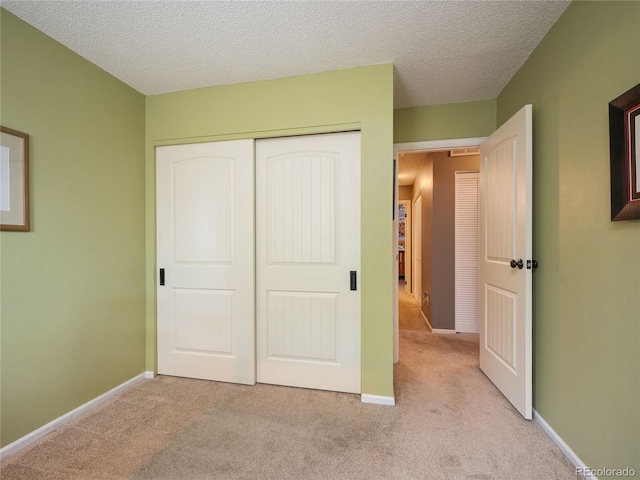 unfurnished bedroom featuring light colored carpet, a textured ceiling, and a closet