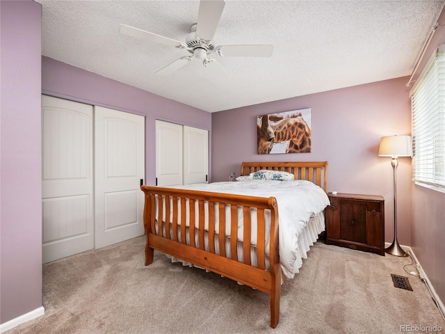 bedroom featuring a textured ceiling, ceiling fan, light colored carpet, and multiple closets