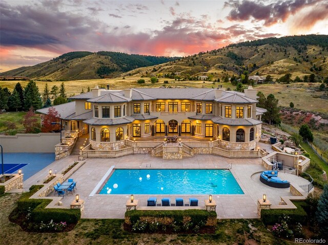 back of property at dusk with a chimney, a mountain view, and a patio