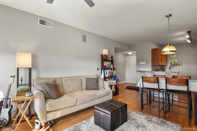 living room with baseboards, wood finished floors, visible vents, and ceiling fan