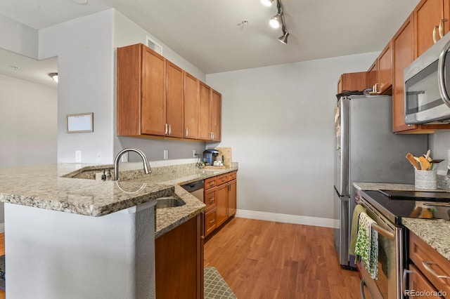 kitchen with a sink, stainless steel appliances, a peninsula, light wood finished floors, and light stone countertops