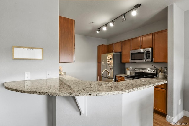 kitchen with light stone counters, appliances with stainless steel finishes, a peninsula, light wood-style floors, and brown cabinetry