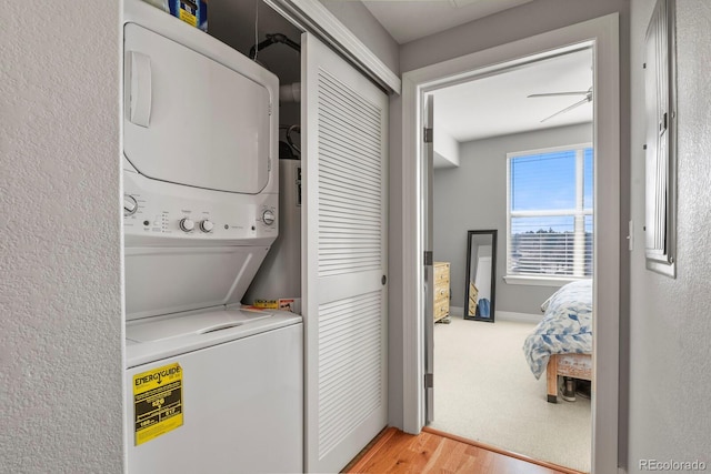 washroom featuring stacked washer / drying machine, baseboards, light wood-style flooring, and laundry area