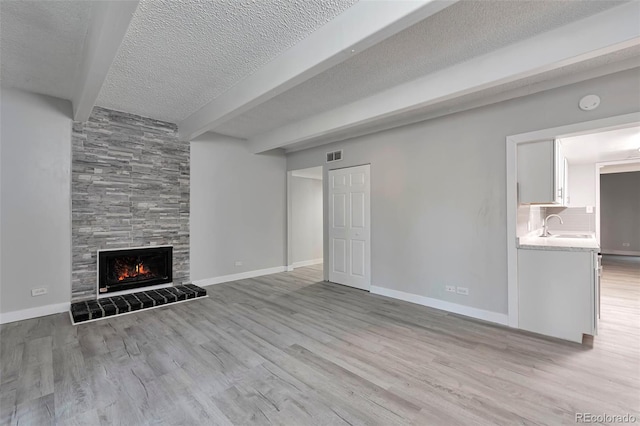 unfurnished living room with a textured ceiling, sink, a tiled fireplace, and light wood-type flooring