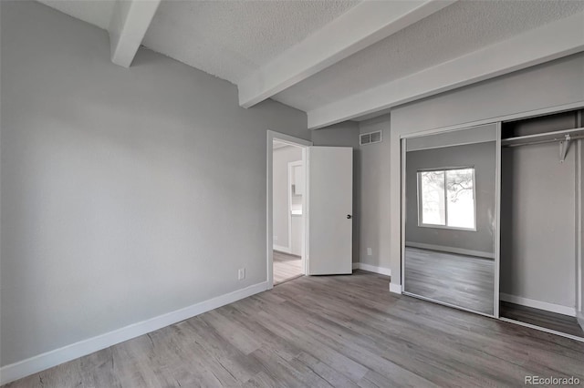 unfurnished bedroom with beam ceiling, wood-type flooring, a closet, and a textured ceiling