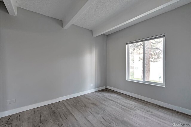 empty room with a textured ceiling, light hardwood / wood-style floors, and beam ceiling