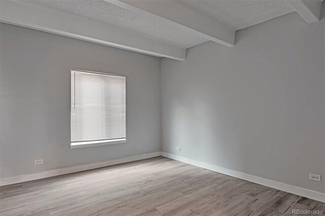 spare room with beamed ceiling, a textured ceiling, and hardwood / wood-style floors