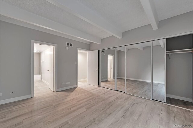 unfurnished bedroom with beamed ceiling, a closet, a textured ceiling, and light hardwood / wood-style floors