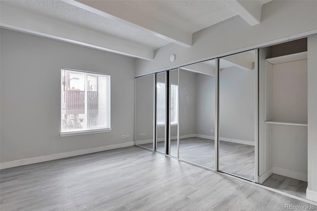 unfurnished bedroom featuring beamed ceiling, a textured ceiling, a closet, and light hardwood / wood-style floors