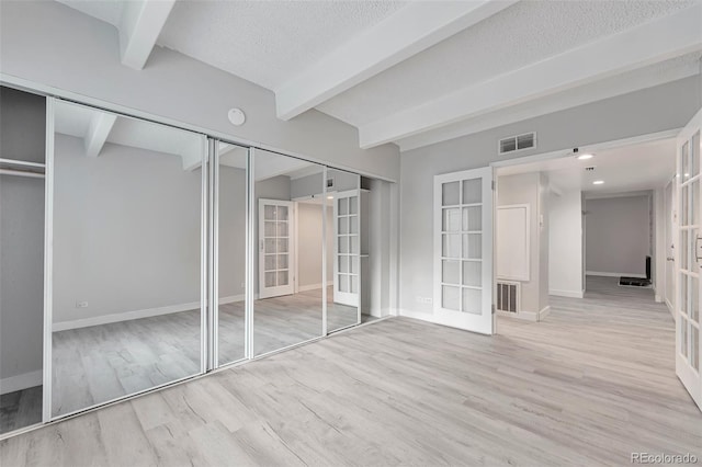 unfurnished bedroom with beamed ceiling, light hardwood / wood-style flooring, and french doors