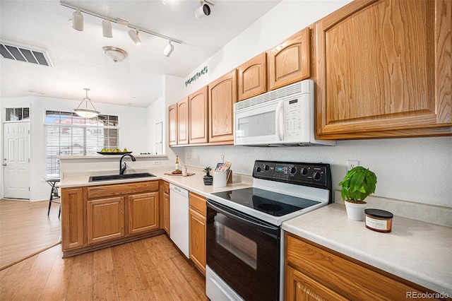 kitchen with kitchen peninsula, hanging light fixtures, sink, white appliances, and light hardwood / wood-style floors