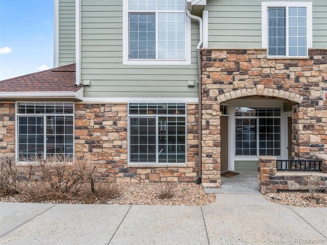 property entrance with stone siding and roof with shingles