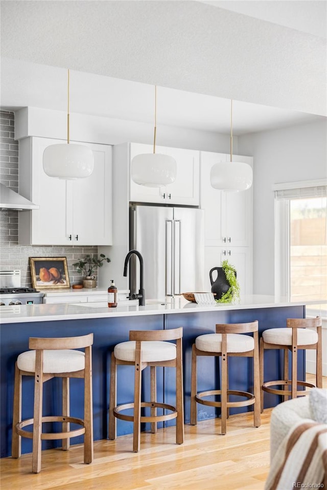 108 Arapahoe St, Golden, CO 80403 - kitchen featuring high end fridge, wall chimney exhaust hood, tasteful backsplash, light wood-type flooring, and a breakfast bar