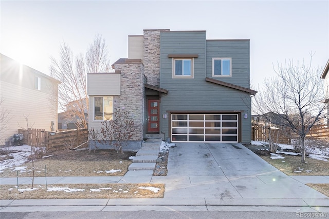 contemporary home featuring driveway, an attached garage, and fence