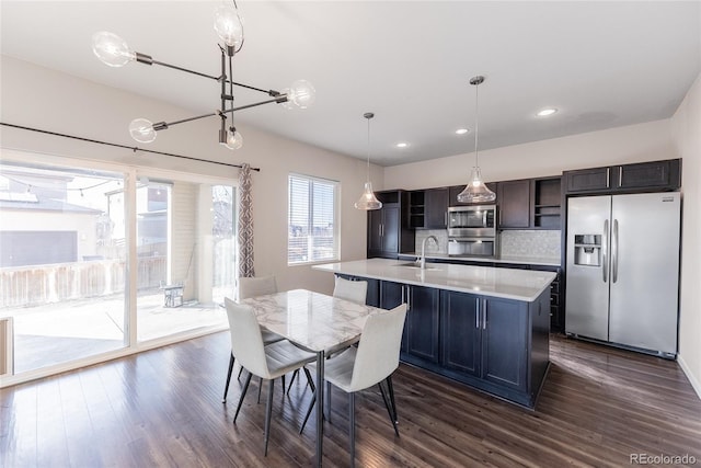 kitchen featuring a sink, light countertops, appliances with stainless steel finishes, a center island with sink, and pendant lighting