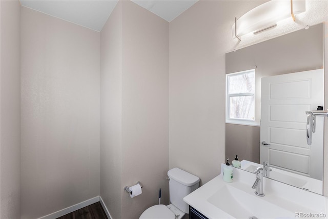 half bathroom featuring wood finished floors, vanity, toilet, and baseboards