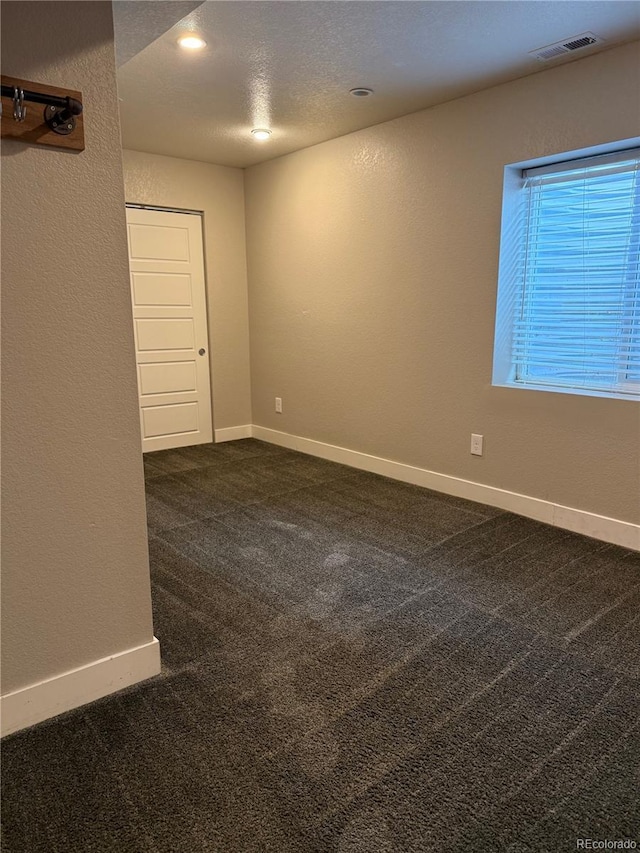 spare room featuring a textured wall, recessed lighting, visible vents, baseboards, and dark colored carpet