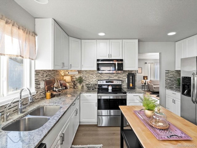 kitchen with a wealth of natural light, white cabinetry, sink, light stone counters, and stainless steel appliances