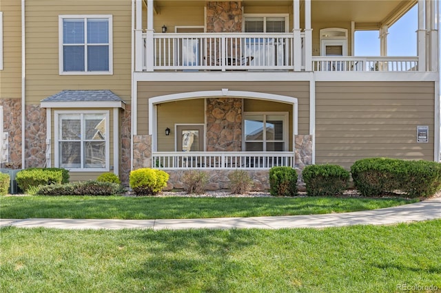 view of front facade with a balcony, stone siding, a porch, and a front yard